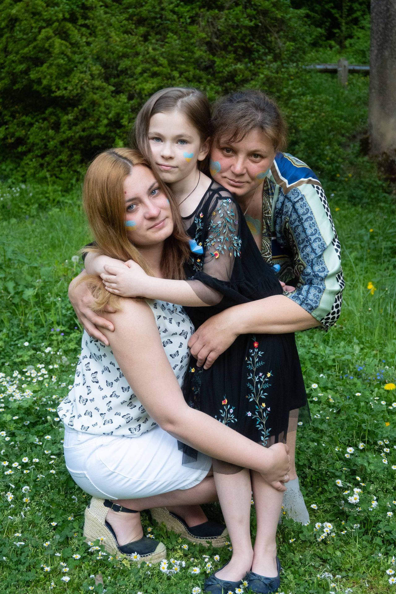 Trois générations d'une même famille enlacées dans un pré fleuri, le bleu et le jaune de l'Ukraine peints sur les joues.